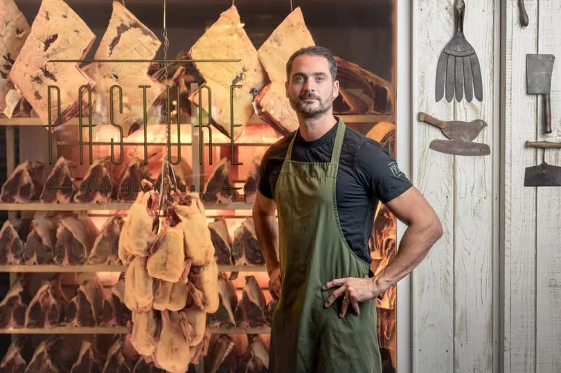 Photo shows Sam in his restaurant with butcher in the background