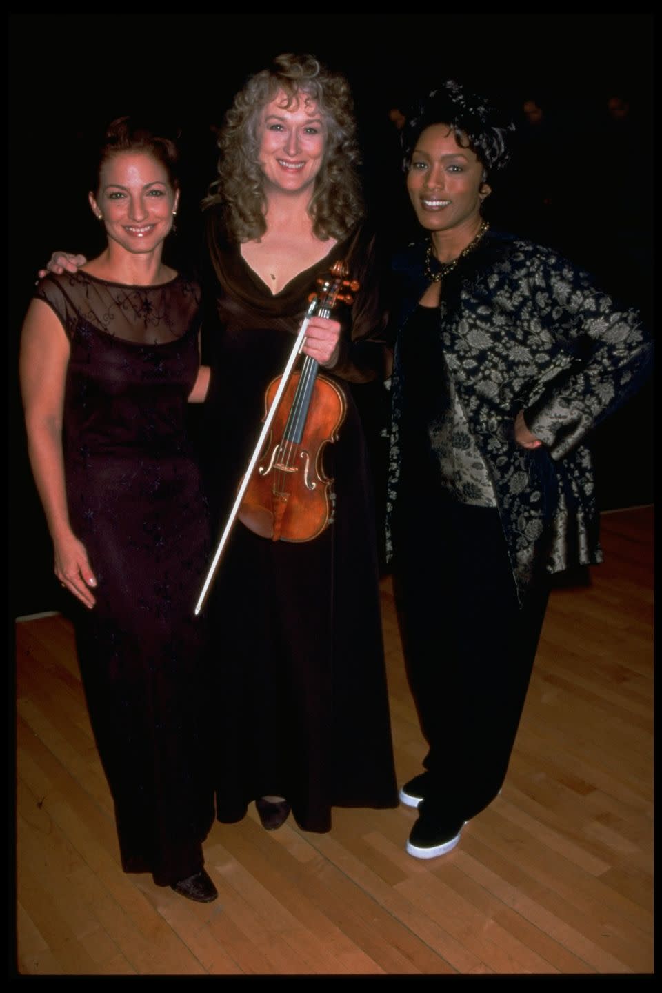 gloria estefan, meryl streep and angela bassett smile for a photo, streep holds a violin in front of her