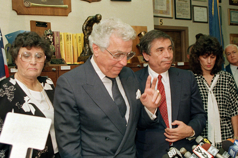 Mario Biaggi holds up his hand while speaking into press microphones. 