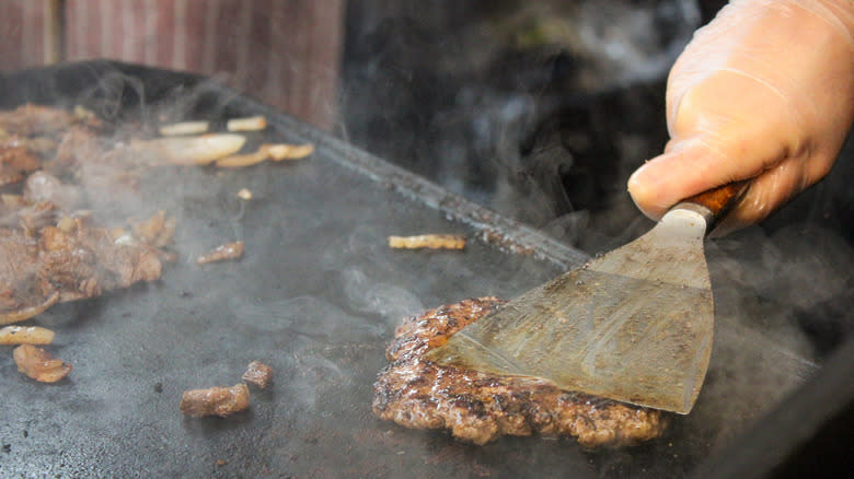 person smashing patties on grill