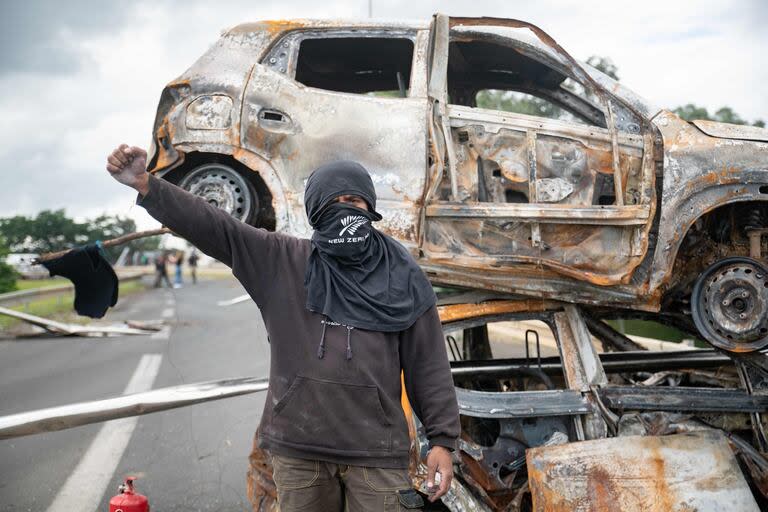 Un transeúnte posa frente a vehículos quemados en un control de carretera a la entrada de Ducos, territorio francés de Nueva Caledonia en el Pacífico, el 21 de mayo de 2024