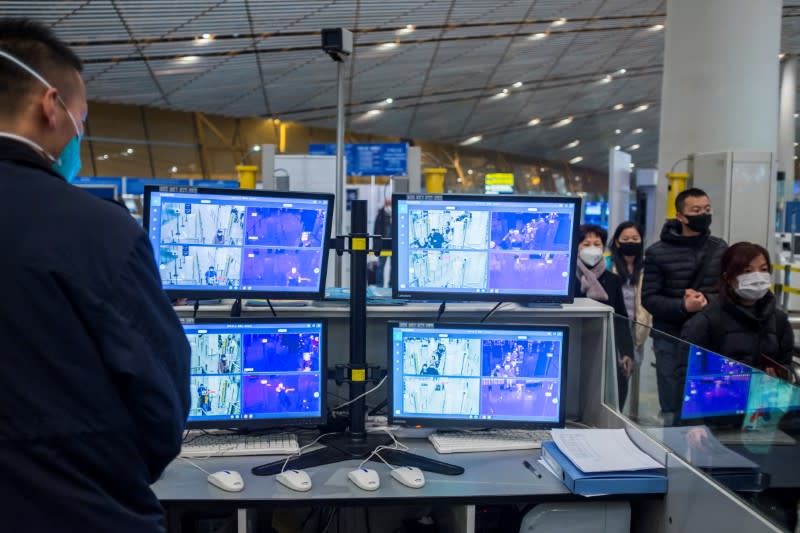 Un funcionario monitorea un escáner térmico mientras personas con mascarillas llegan al Aeropuerto Internacional en Pekín.