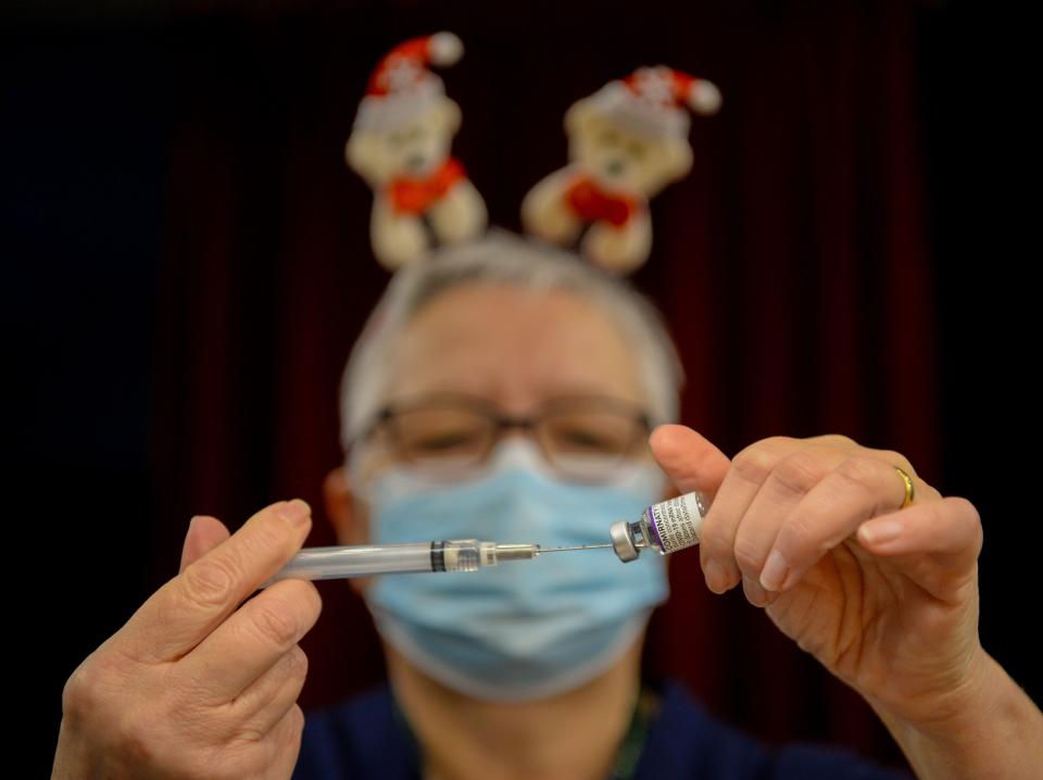Person with santa headband prepares injection for booster dose.