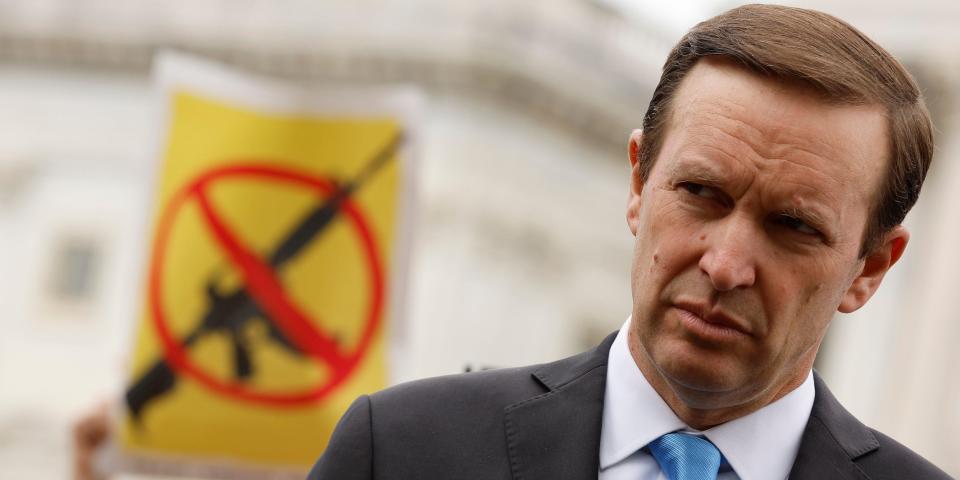 Chris Murphy stands in front of an anti-assault weapon sign depicting an AR-15.