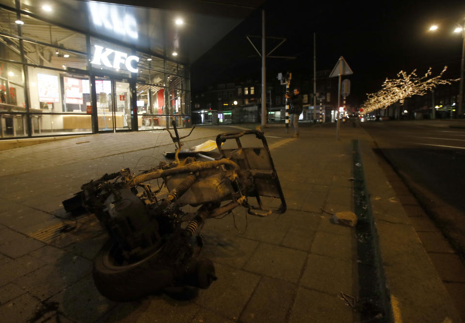 The burned wreck of a motor scooter lays on the pavement outside a fast-food restaurant that had it's windows smashed in protests against a nation-wide curfew in Rotterdam, Netherlands, Monday, Jan. 25, 2021. The Netherlands Saturday entered its toughest phase of anti-coronavirus restrictions to date, imposing a nationwide night-time curfew from 9 p.m. until 4:30 a.m. in a bid to control the COVID-19 infection rate. (AP Photo/Peter Dejong)