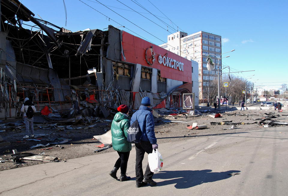 A couple in winter jackets pass a store that was damaged by shelling.