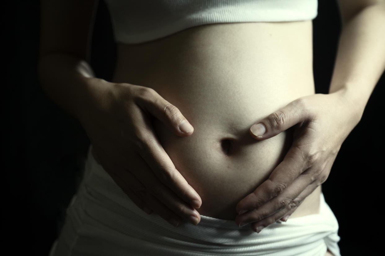 pregnant woman holding her stomach in front of a black background