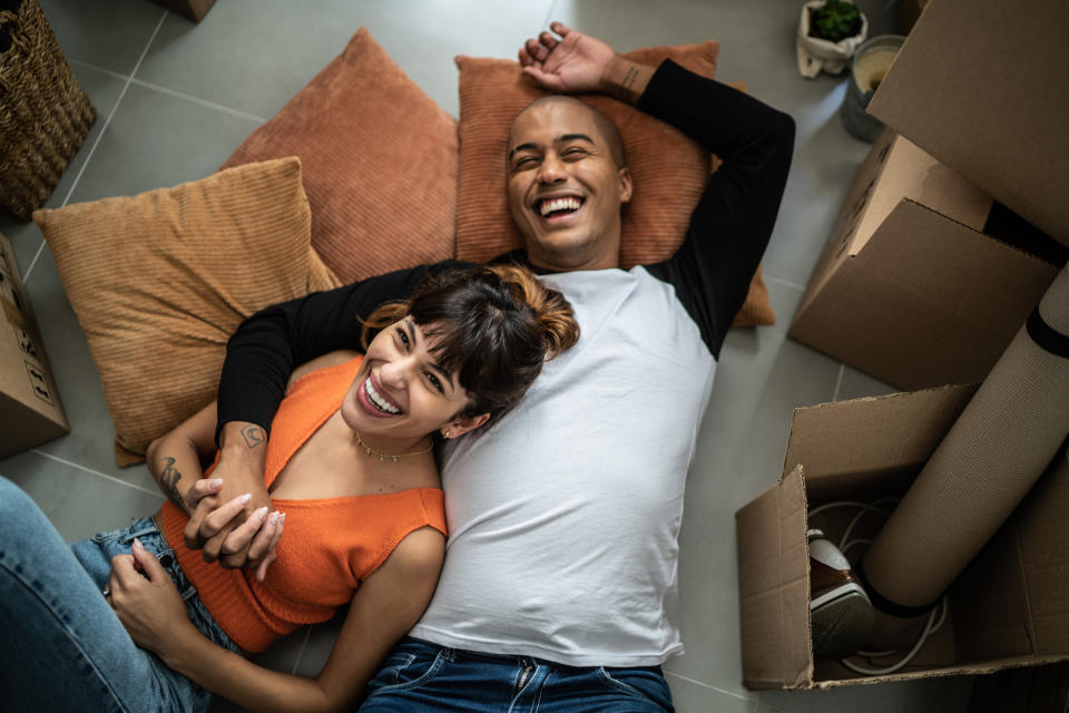 Couple laughing on floor among moving boxes, possibly celebrating new life chapter after wedding