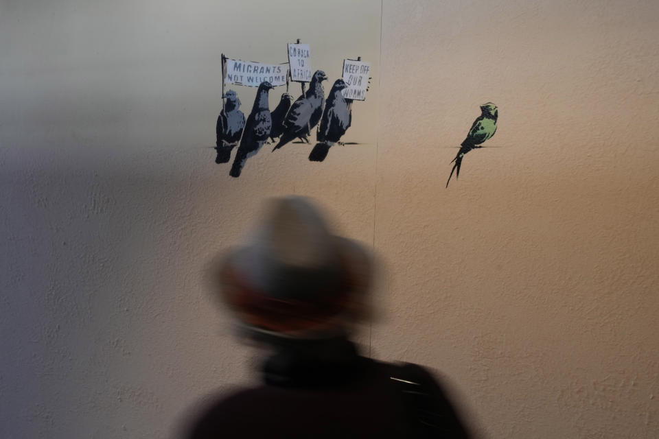 A visitor walks past "Pigeons", a reproduction of a mural by British artist Banksy, during the unveiling of the "The World of Banksy, The Immersive Experience" exhibition, in Milan, Italy, Thursday, Dec. 2, 2021. An exhibition of 130 works by British street artist Banksy opens Friday in a gallery space inside Milan's Central train Station. The exhibition unveiled on Thursday includes 30 never before seen works by Bansky and highlights pieces by young unknown artists from all over Europe. (AP Photo/Luca Bruno)