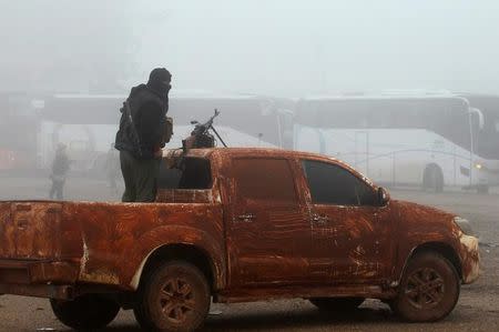 A rebel fighter stands on a vehicle near buses carrying people that evacuated from the two villages of Kefraya and al-Foua, after an agreement reached between rebels and Syria's army, at insurgent-held al-Rashideen, Aleppo province, Syria April 14, 2017. REUTERS/Ammar Abdullah