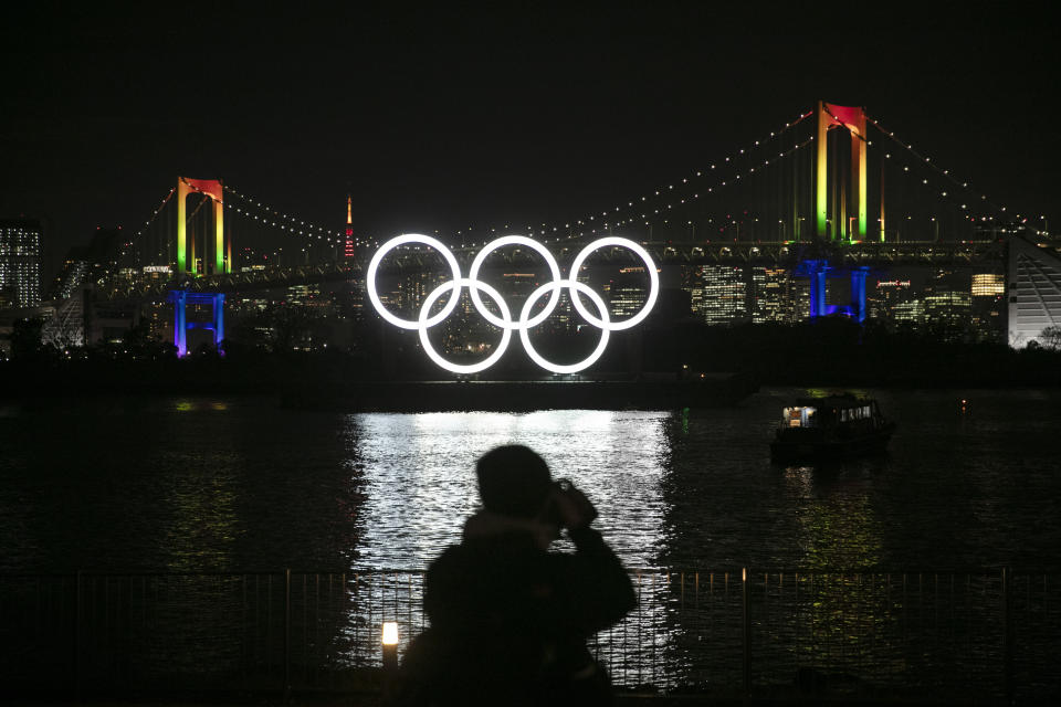 A photographer takes pictures of the illuminated Olympic rings in front of the Rainbow Bridge Friday, Jan. 24, 2020, in the Odaiba district of Tokyo. Tokyo put on a flashy fireworks display on Friday to mark the 6-months-to-go milestone for this summer's Olympics. (AP Photo/Jae C. Hong)