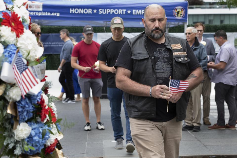 Brian Abelli, foreground, walks past a wreath in memory of Marine Sgt. Johanny Rosario Pichardo from Lawrence, Mass., after placing a rose at the Massachusetts Fallen Heroes Memorial, Saturday, Aug. 28, 2021, in Boston. The ceremony was held to honor the U.S. service members killed in a suicide bombing at the airport in Kabul, Afghanistan, including Sgt. Rosario Pichardo. (AP Photo/Michael Dwyer)