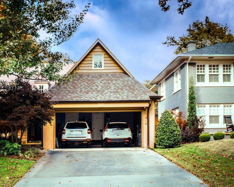 Two car garage open with two white SUVS parked inside on autumn day