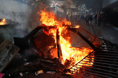 Demonstrators stand close to the remains of a burning car used as barricade during a protest near to a National Guard outpost in Caracas, Venezuela January 21, 2019. REUTERS/Carlos Garcia Rawlins