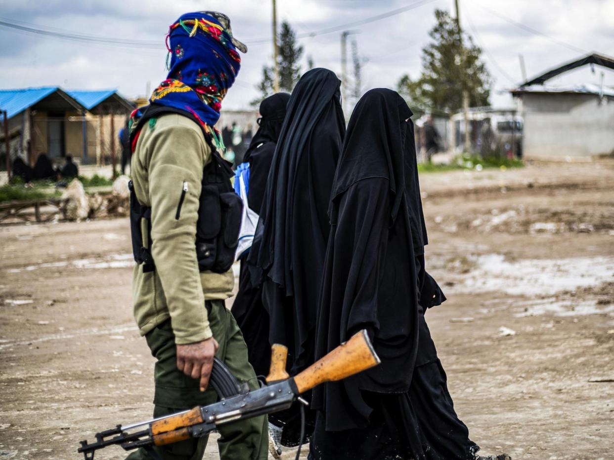 Foreign women living in al-Hol camp, which houses relatives of Isis members, walk under the supervision of a fighter of the Syrian Democratic Forces on 28 March 2019: AFP