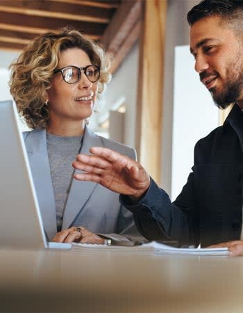 A man and a woman chat while looking at a laptop screen.