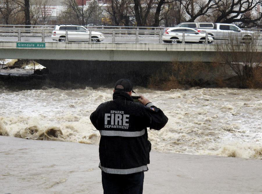 A Sparks firefighter takes a picture of the rising Truckee River, Sunday, Jan. 8, 2017, where it runs near the Grand Sierra hotel-casino along a line that divides the cities of Reno and Sparks, Nev. More than 1,000 homes have been evacuated due to overflowing streams and drainage ditches in the area, which remains under a flood warning through Tuesday. (AP Photo/Scott Sonner)