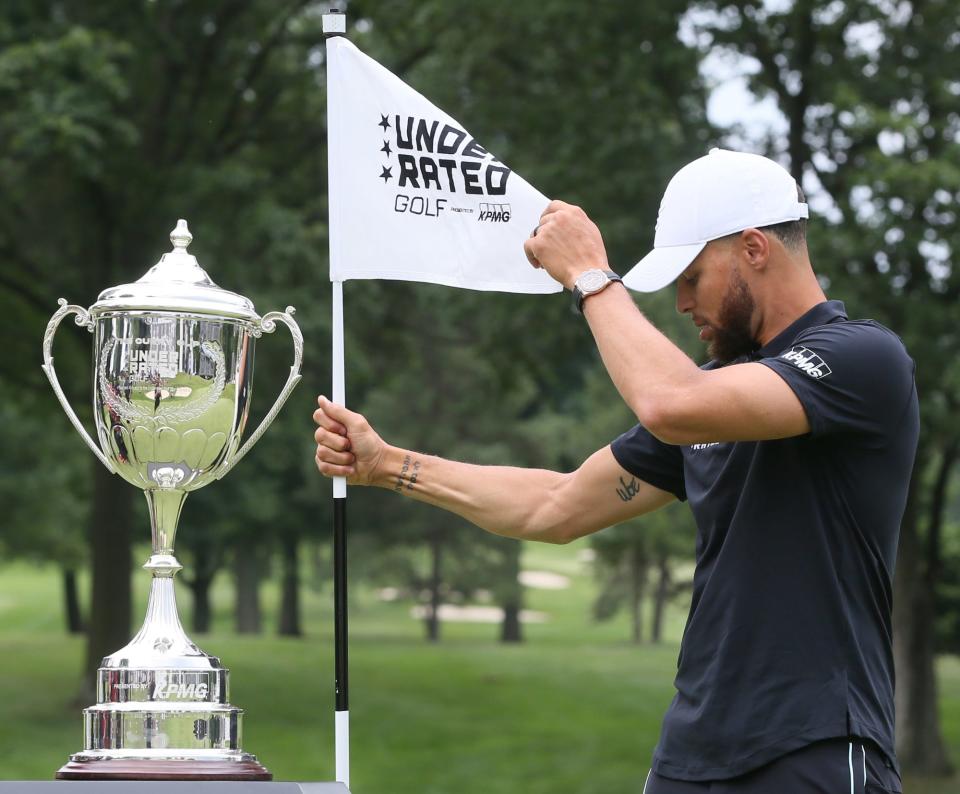 Stephen Curry straightens out the flag as he helps get the trophy ceremony area ready during Underrated Golf tour on the South Course at Firestone Country Club in Akron.