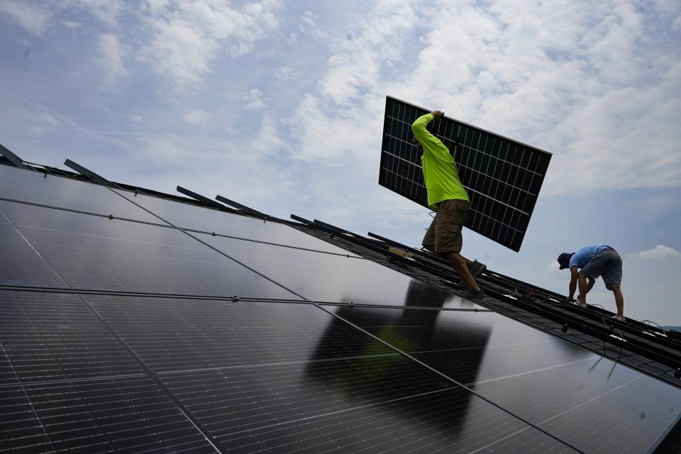 FILE - Nicholas Hartnett, owner of Pure Power Solar, carries a panel as he and Brian Hoeppner, right, install a solar array on the roof of a home in Frankfort, Ky., Monday, July 17, 2023. President Joe Biden has been careful not to declare an outright victory against inflation, but the White House says the cost savings from the Inflation Reduction Act are coming as the law is getting enacted. Tax credits will reduce the cost of installing rooftop solar panels by 30%, which will in turn lower monthly electricity bills. (AP Photo/Michael Conroy, File)