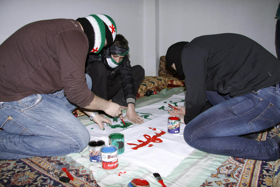 FILE-In this March 21, 2012, file photo, anti-Syrian regime activists cover their faces with scarves in the colors of the Syrian revolution flag as they prepare a banner to be held in a protest, in Damascus, Syria. Last year, Abu Bakr Saleh was a 19-year-old Syrian university student whose modest dreams were to land a job and earn enough to marry his girlfriend _ not simple tasks given Syria's weak economy and his lack of connections to the ruling elite. Many youth activists say they had plenty to revolt about as they faced adulthood in societies where decades of autocratic rule left them with limited freedoms and constricted economies. For Saleh and other young Syrian activists, the uprising is about more than toppling a dictator. It's fight for their generation's dreams. (AP Photo, File)