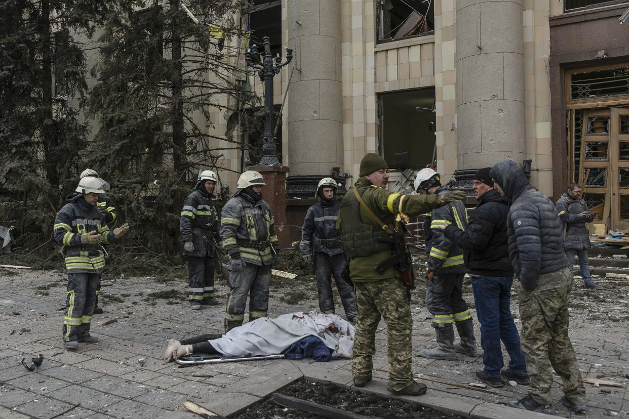 Ukrainian emergency service personnel and servicemen stand around a body of a victim following shelling of the City Hall building in Kharkiv, Ukraine, Tuesday, March 1, 2022. Russia on Tuesday stepped up shelling of Kharkiv, Ukraine's second-largest city, pounding civilian targets there. Casualties mounted and reports emerged that more than 70 Ukrainian soldiers were killed after Russian artillery recently hit a military base in Okhtyrka, a city between Kharkiv and Kyiv, the capital.