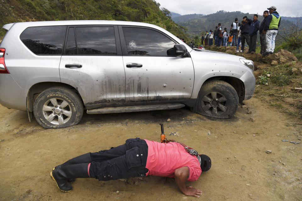 A man looks under a car riddled by bullets on the road leading to Tacueyo, in southwest Colombia, Wednesday, Oct. 30, 2019. Five indigenous leaders of the Tacueyo reservation were killed late Tuesday when the two vehicles they were traveling in were ambushed by gunmen the government says are part of a dissident front of Revolutionary Armed Forces of Colombia.(AP Photo/Christian Escobar Mora)