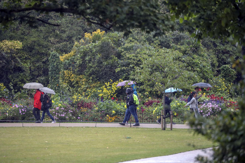 People use umbrellas to cover from the rain in St James's Park, London.