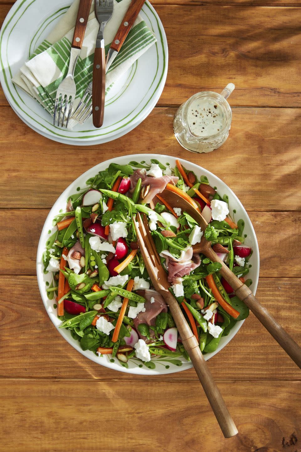 snap pea salad with feta, almonds, and prosciutto in a large white bowl with wooden serving utensils