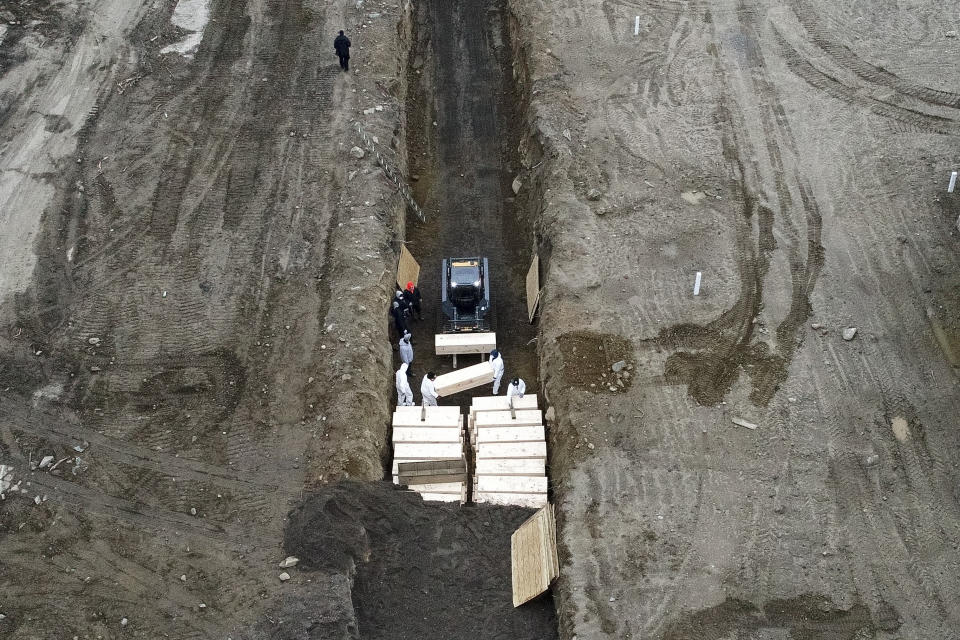 Workers wearing personal protective equipment bury bodies in a trench on Hart Island, Thursday, April 9, 2020, in the Bronx borough of New York. On Thursday, New York City’s medical examiner confirmed that the city has shortened the amount of time it will hold on to remains to 14 days from 30 days before they will be transferred for temporary internment at a City Cemetery. Earlier in the week, Mayor Bill DeBlasio said that officials have explored the possibility of temporary burials on Hart Island, a strip of land in Long Island Sound that has long served as the city’s potter’s field. (AP Photo/John Minchillo)