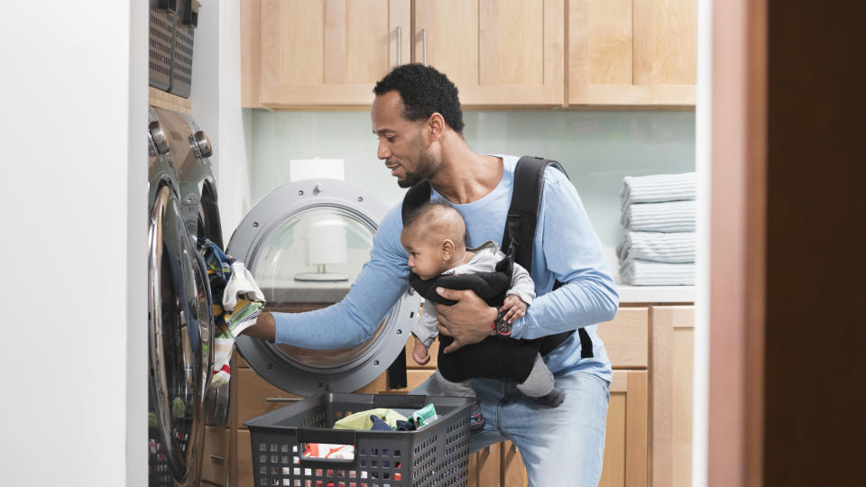 A father with a baby in a carrier doing laundry