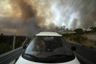 A dog sits inside a car as wildfire burns in Agios Stefanos, in northern Athens, Greece, Friday, Aug. 6, 2021. Thousands of people have fled wildfires burning out of control in Greece and Turkey, including a major blaze just north of the Greek capital of Athens that left one person dead. (AP Photo/Petros Karadjias)