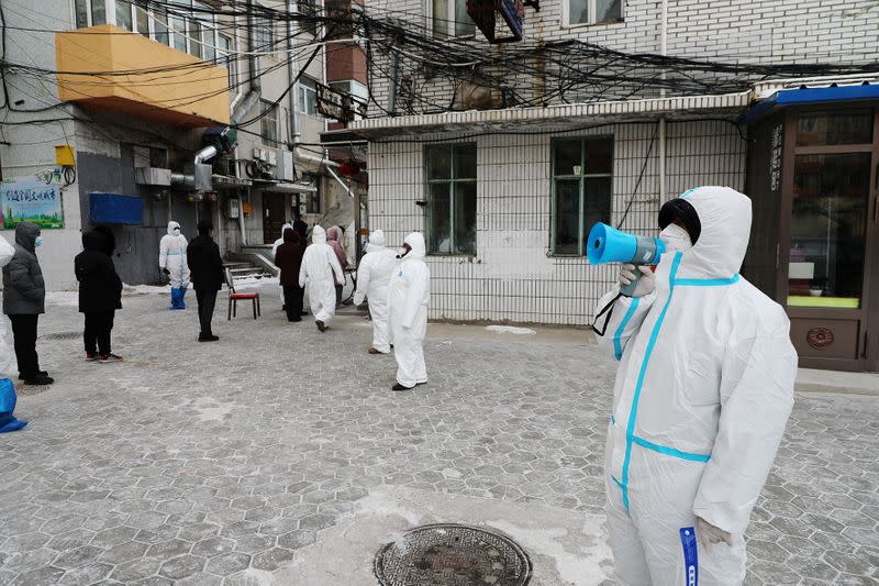 A staff member in a protective suit uses a speaker to guide residents to line up for a nucleic acid test for COVID-19 following new cases, in Manzhouli