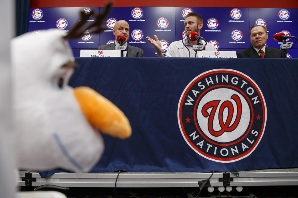 Washington Nationals pitcher Stephen Strasburg, center, speaks during a base media availability, accompanied by general manager Mike Rizzo, left, and agent Scott Boras, right, with Strasburg's daughter's stuffed toy at left, at Nationals Park, Tuesday, Dec. 17, 2019, in Washington. (AP Photo/Alex Brandon)