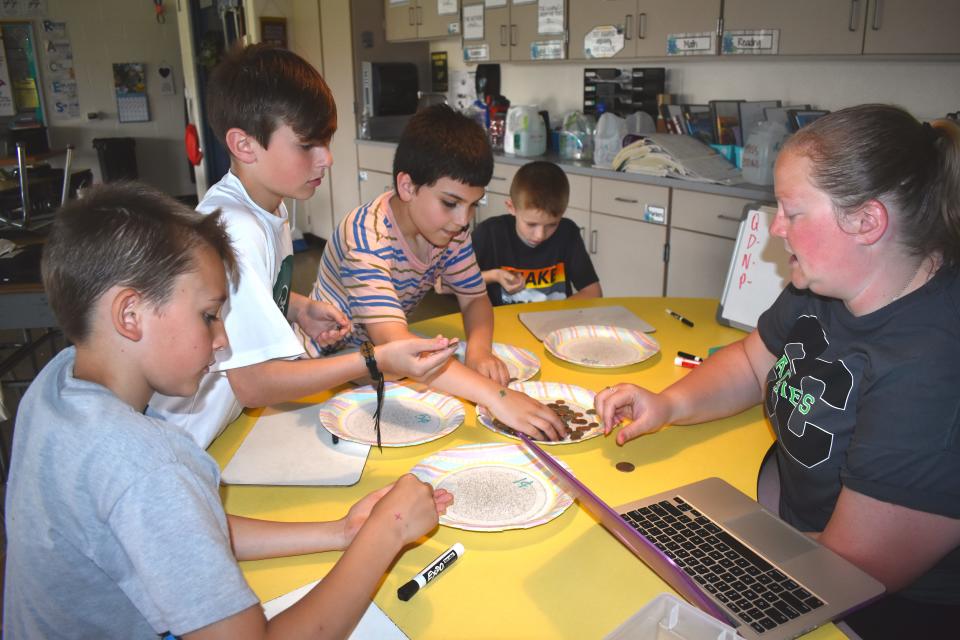 Fourth grade students at Ruth McGregor Elementary School in Sand Creek, from left, Caden Brewer, Emerson Walsh, Damien Salerno and Jackson Smith count up coins with the assistance of teacher Caitlyn Hella Friday during the final day of the elementary school's Money Wars fundraiser. The entire school participated in the weeklong fundraiser last week and generated $3,462.67 to purchase new playground equipment for the elementary school.