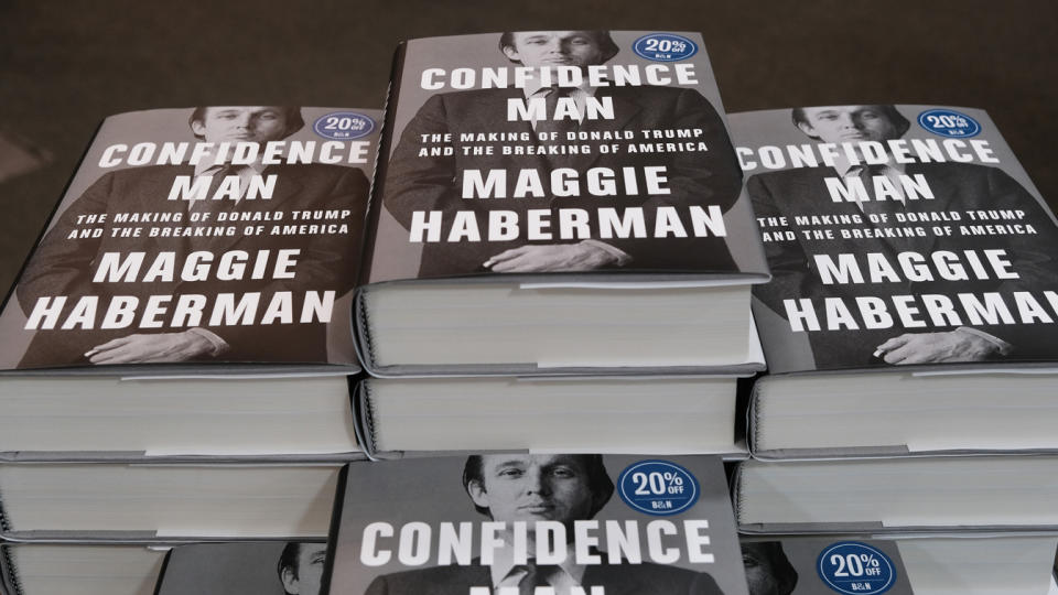 Stacks of books with a dust jacket that has picture of a young Donald Trump and reading: Confidence Man, the making of Donald Trump and the breaking of America, Maggie Haberman