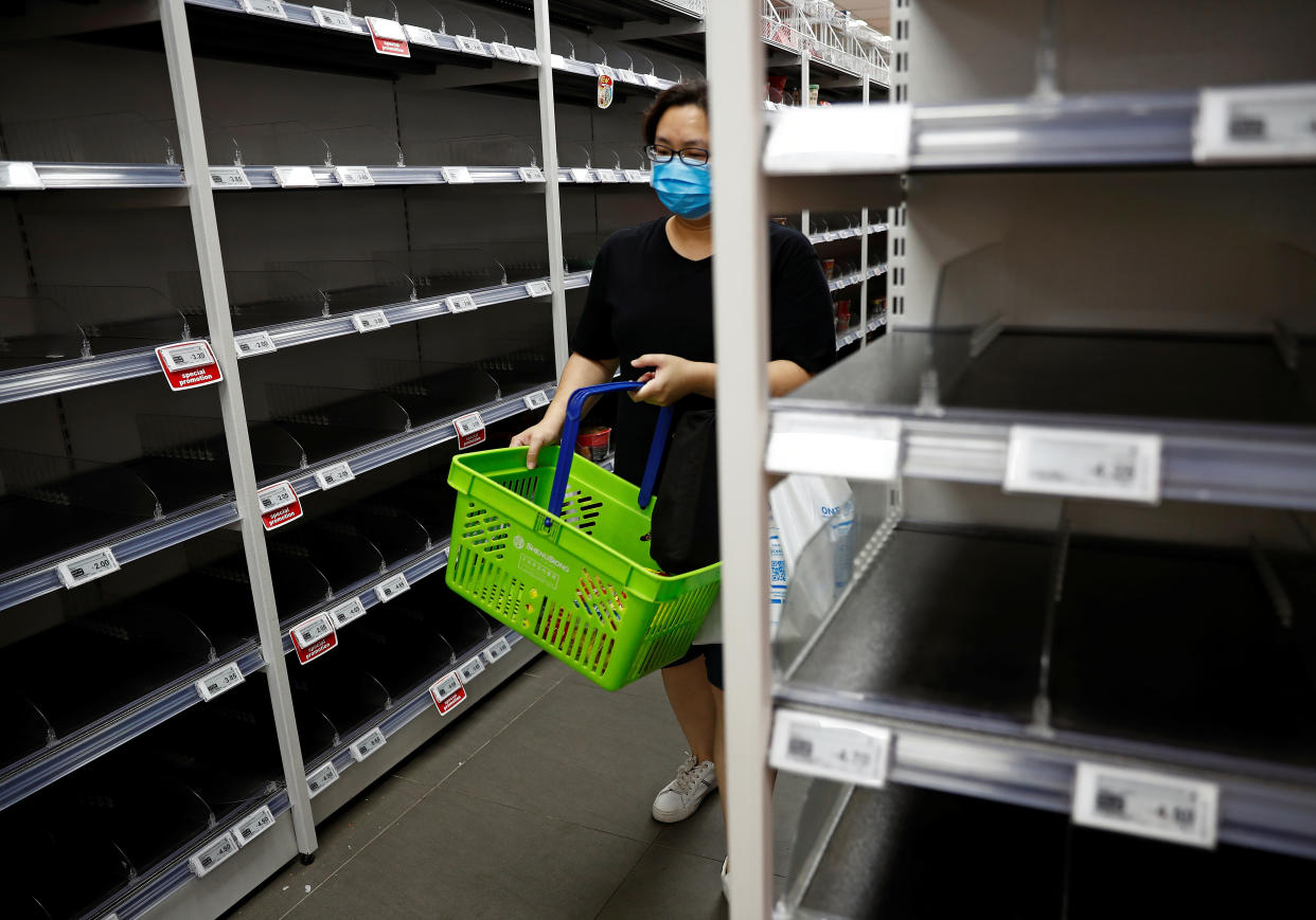 A woman wearing a protective mask passes empty shelves of instant noodles and canned food as people stock up on food supplies after Singapore raised coronavirus outbreak alert level to orange, at a supermarket in Singapore on 8 February, 2020. (PHOTO: Reuters)