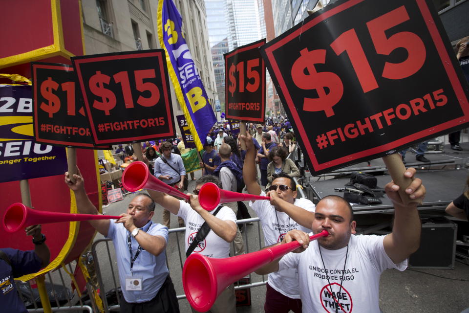People in the streets blow horns and raise signs that say '$15 #FIGHTFOR15' 