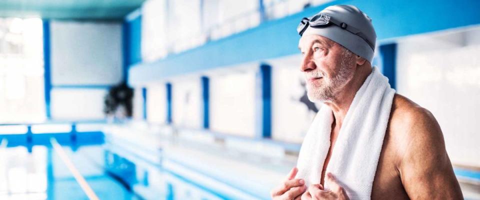 Senior man standing by the indoor swimming pool.