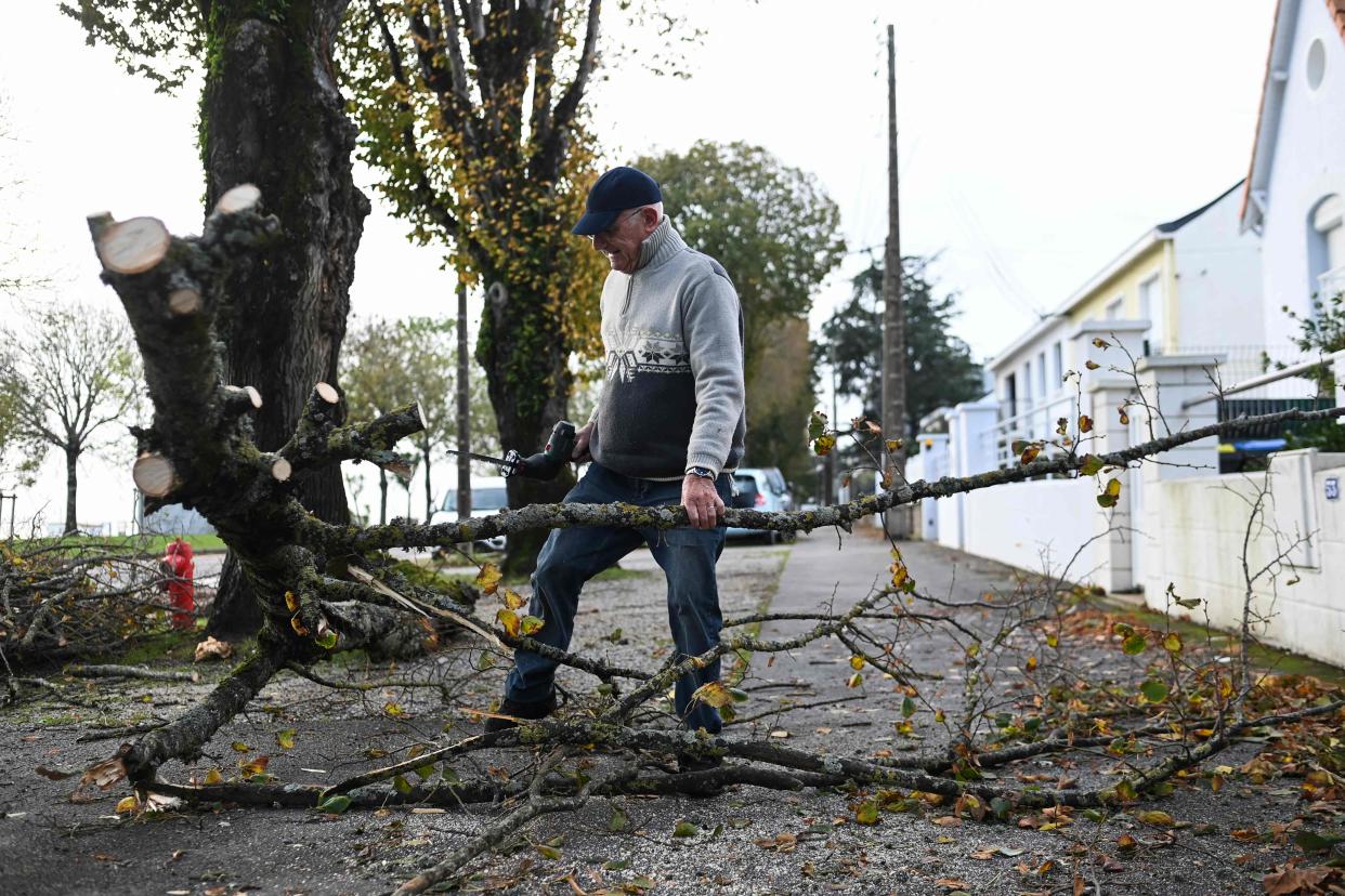 A retired man cuts a fallen tree in front of his house in Saint-Nazaire, western France (AFP via Getty Images)