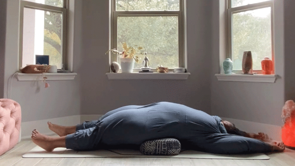 Woman stretching her hips, low back, and shoulders while lying on her back in her bedroom