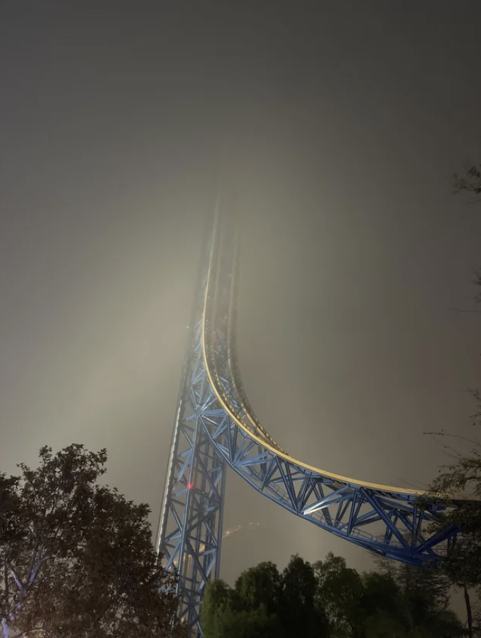 A roller coaster disappearing into a foggy nighttime sky