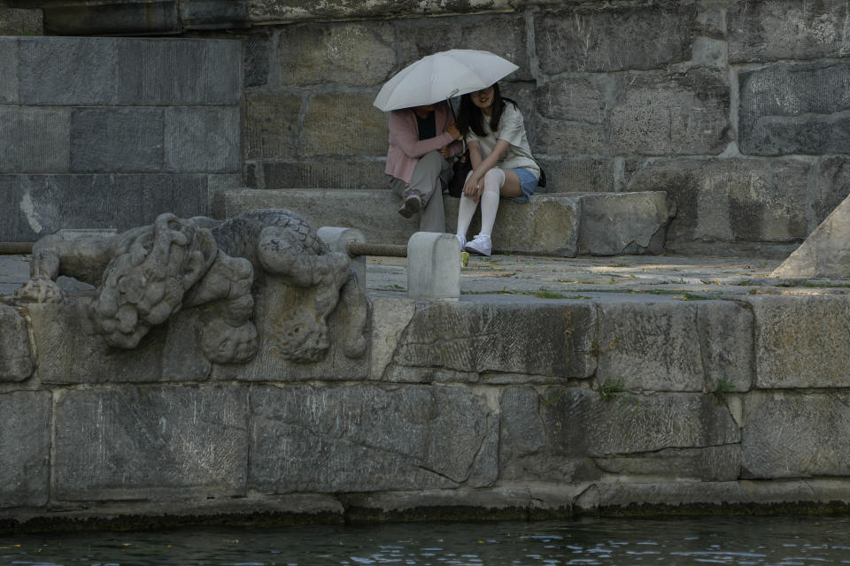 Women hold an umbrella take a rest in the shade in a hot and sunny day in Beijing, Sunday, June 16, 2024. China is being buffeted by two weather extremes, with heavy rain and flooding in parts of the south and a heat wave and potential drought in the north. (AP Photo/Andy Wong)