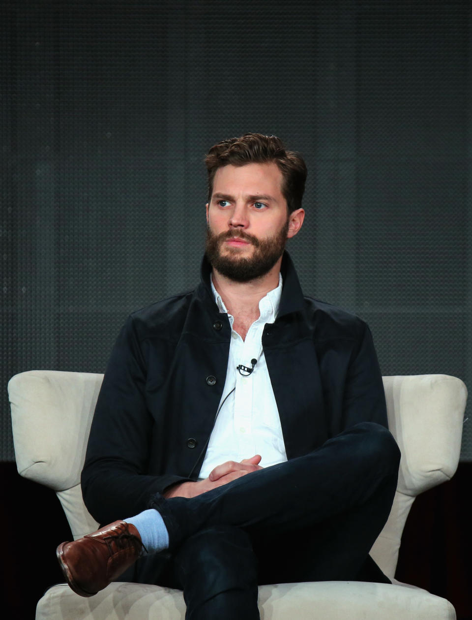 Jamie Dornan seated onstage with crossed legs