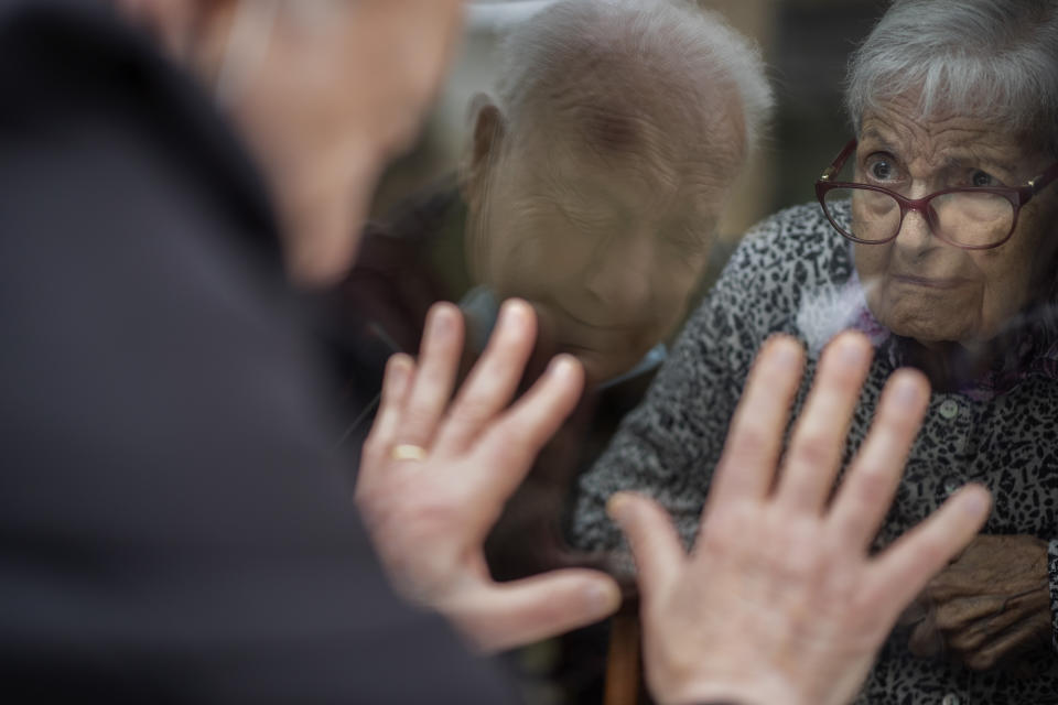 FILE - Javier Anto, 90, reacts in front of his wife Carmen Panzano, 92, through the window separating the nursing home from the street in Barcelona, Spain, on April 21, 2021. The World Health Organization said Friday May 5, 2023 that COVID-19 no longer qualifies as a global emergency, marking a symbolic end to the devastating coronavirus pandemic that triggered once-unthinkable lockdowns, upended economies and killed millions of people worldwide. (AP Photo/Emilio Morenatti, File)