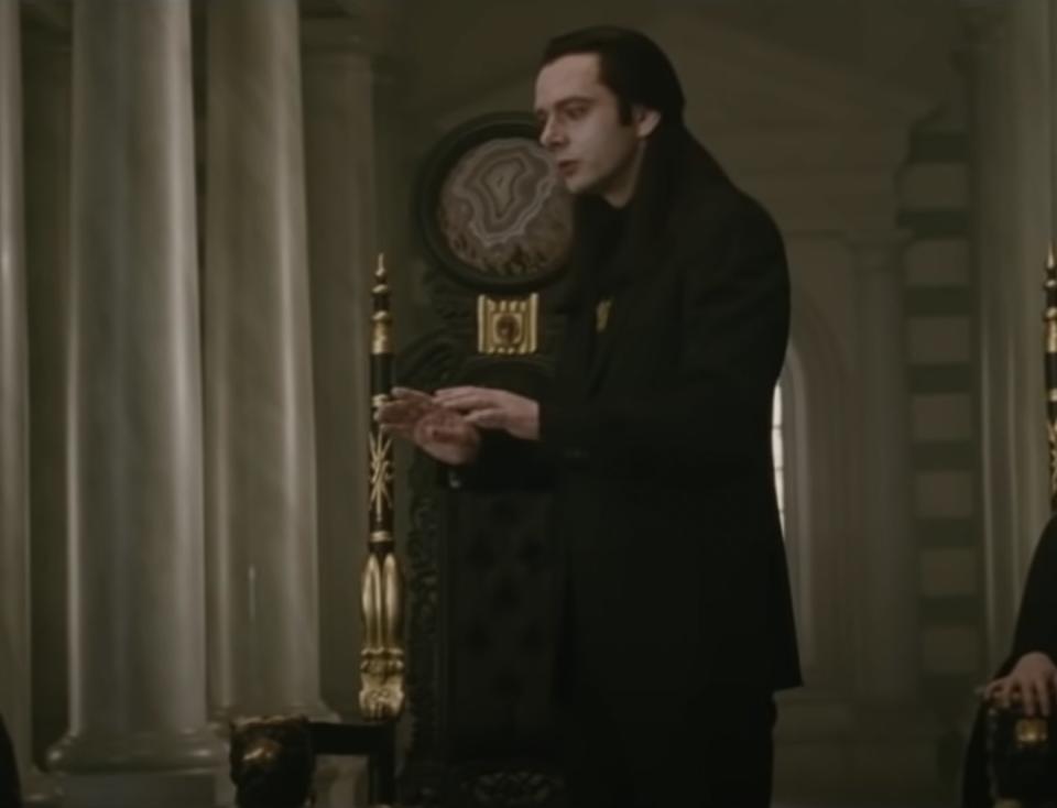 Aro wearing a suit over a shirt with a high collar and a necklace