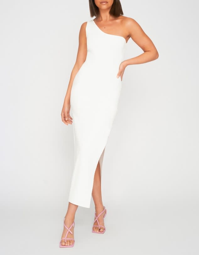 A model wears a white By Johnny, One Shoulder Grace Full Length Dress, $390 against a pale background with strappy high heels.