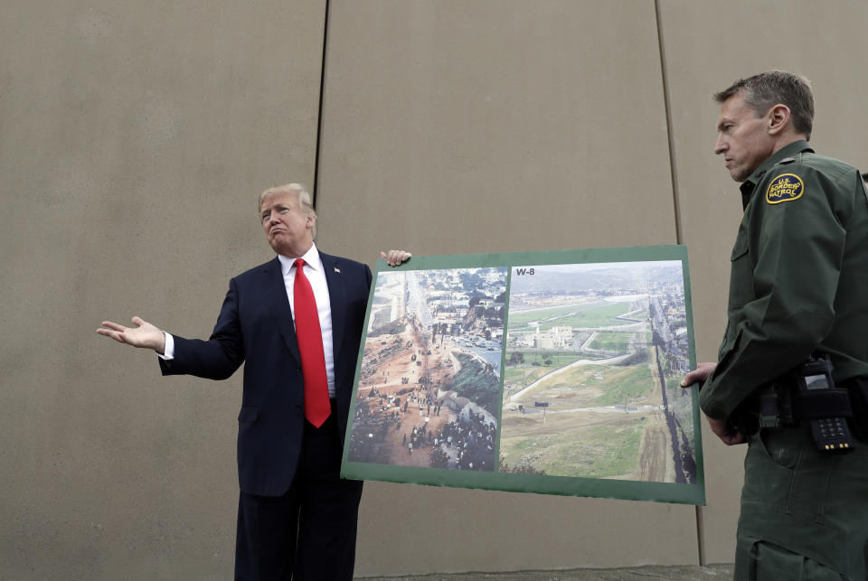 FILE - In this March 13, 2018, file photo, President Donald Trump holds a poster with photographs of the U.S. - Mexico border area as he reviews border wall prototypes in San Diego with Rodney Scott, the U.S. Border Patrol's San Diego sector chief. The Trump administration on Wednesday, Feb. 27, 2019, began demolishing eight prototypes of the president's prized border wall, saying they have served their purpose. (AP Photo/Evan Vucci, File)