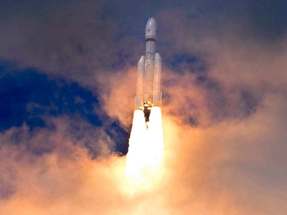 white rocket with two boosters on its sides launches through clouds with flames shooting out of boosters