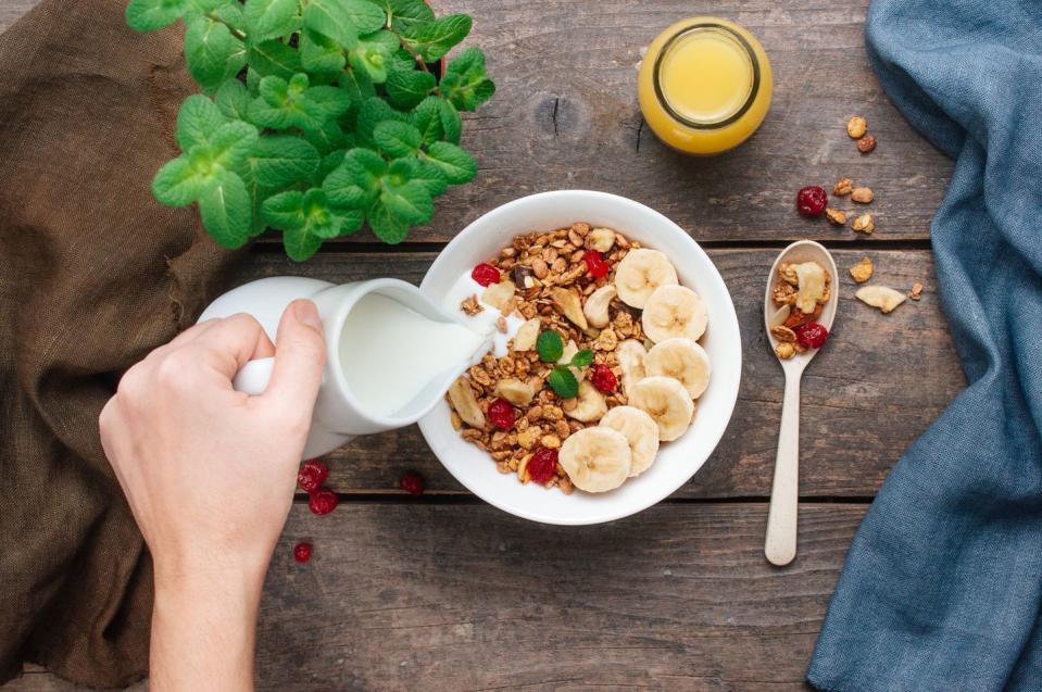 close up of woman pouring milk into bowl with granola