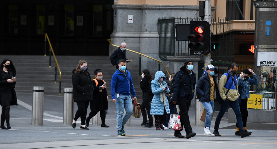 A small crowd of people pictured walking along a Melbourne street, some wearing masks. Source: AAP